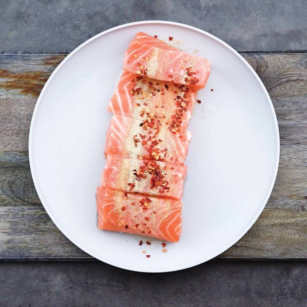 Salmon fillets with seasonings on a plate.