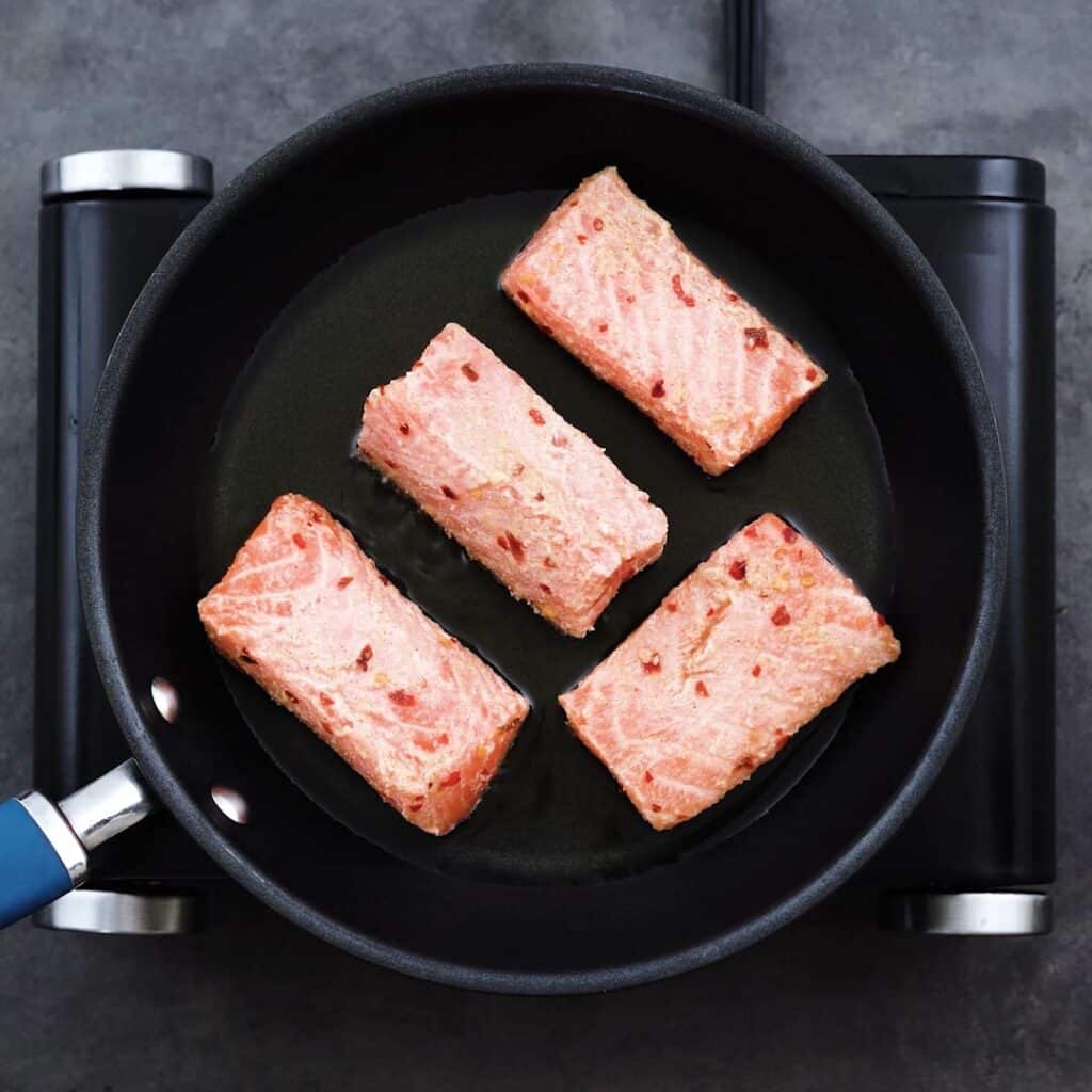 Salmon fillets searing in a frying pan.