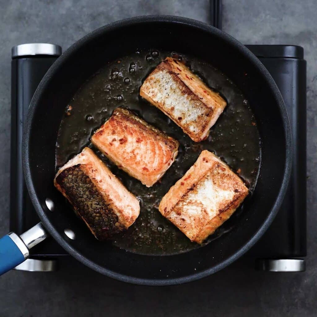 Crispy skin on salmon fillets searing in a frying pan.