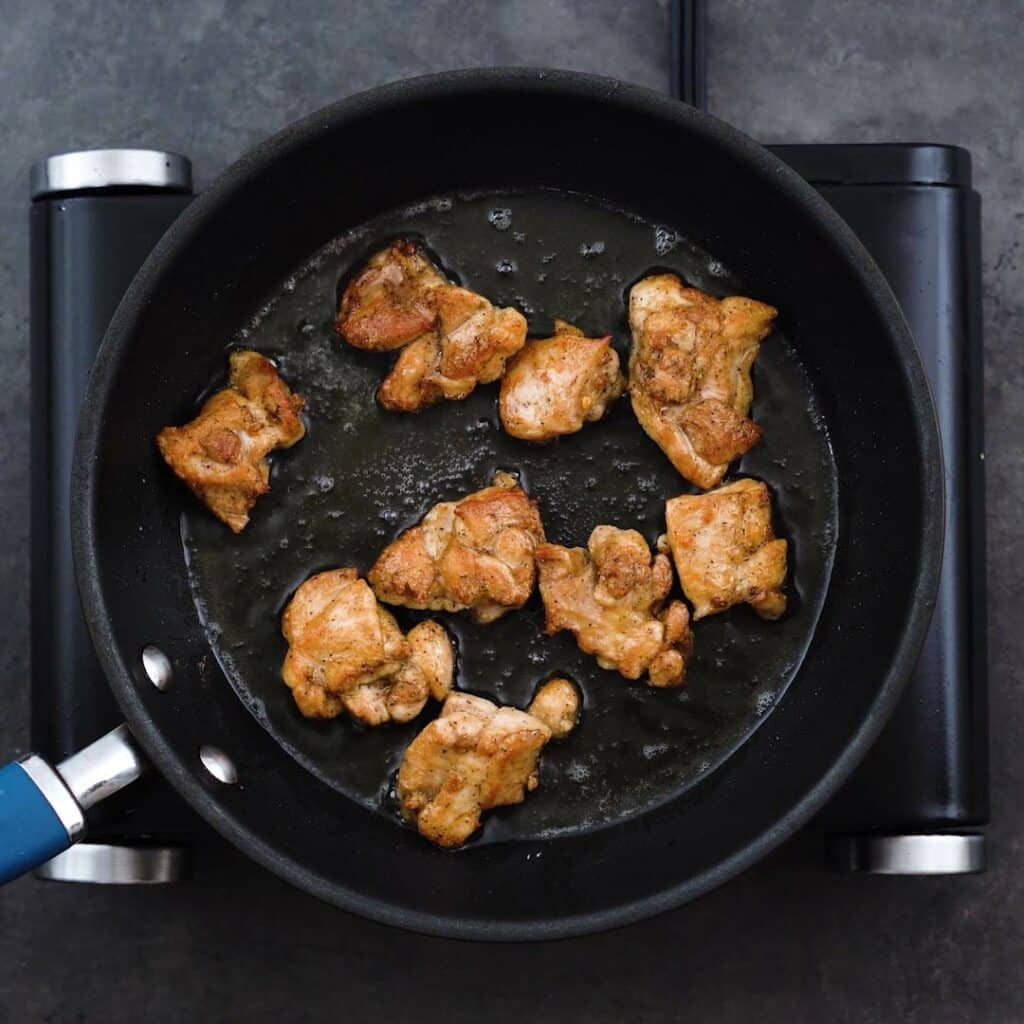Golden fried chicken thighs in a frying pan.