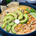 White chicken chili in a blue bowl with avocado, lime and tortilla chips.