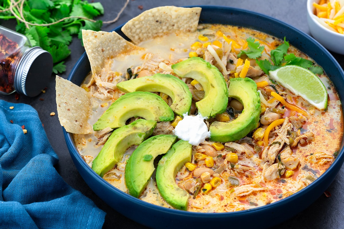 White chicken chili in a blue bowl with avocado, lime and tortilla chips.