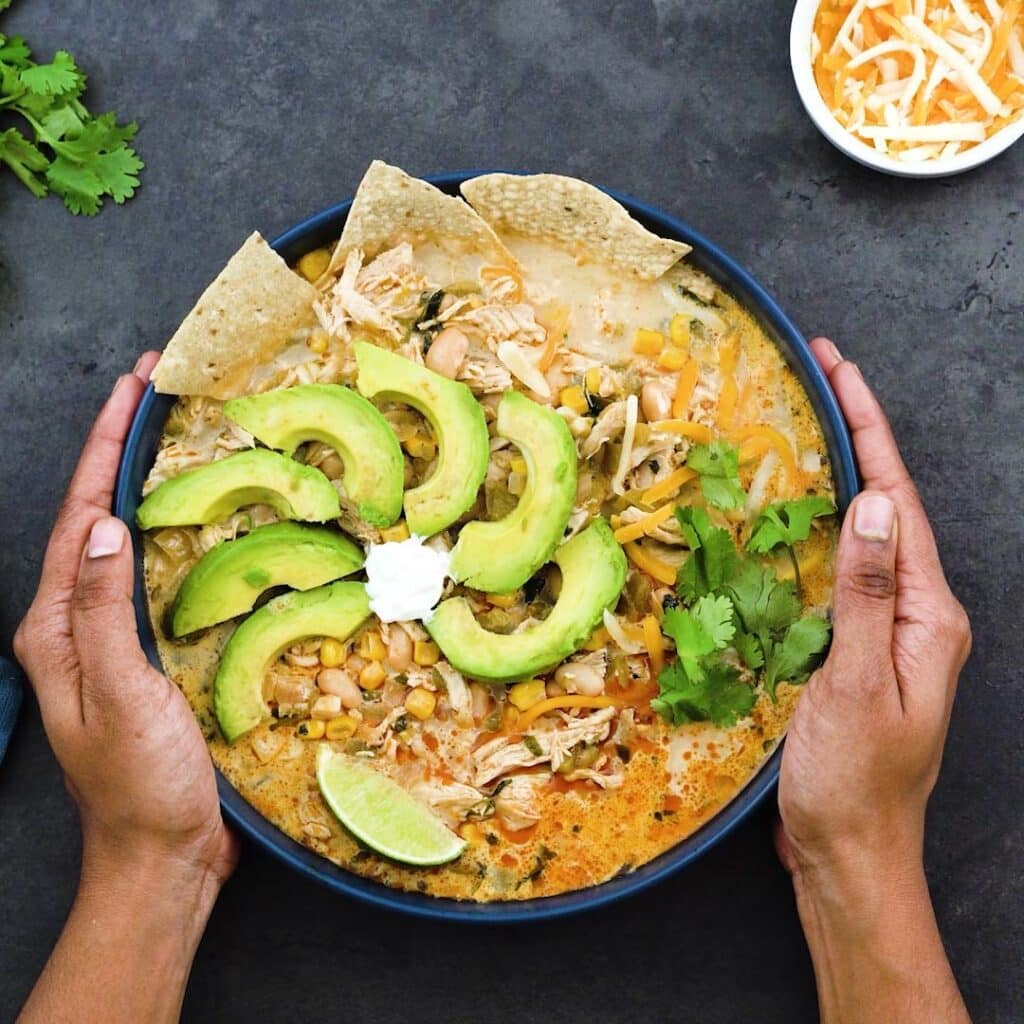 Serving White Chicken Chili with avocado, tortilla chips,sour cream, lime wedges and coriander leaves.