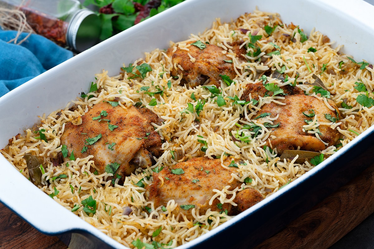 Baked chicken and rice in a backing tray with few ingredients around.