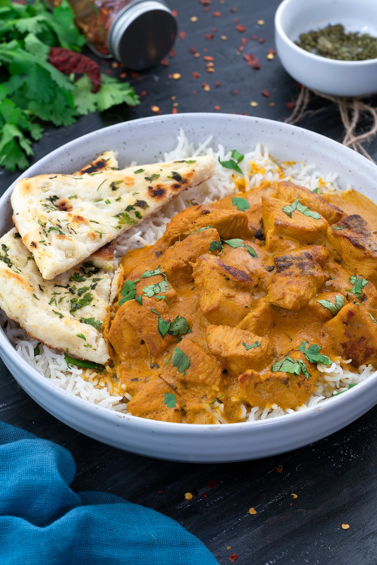 Butter chicken curry served in a bowl with rice and naan, and a few ingredients on the side.