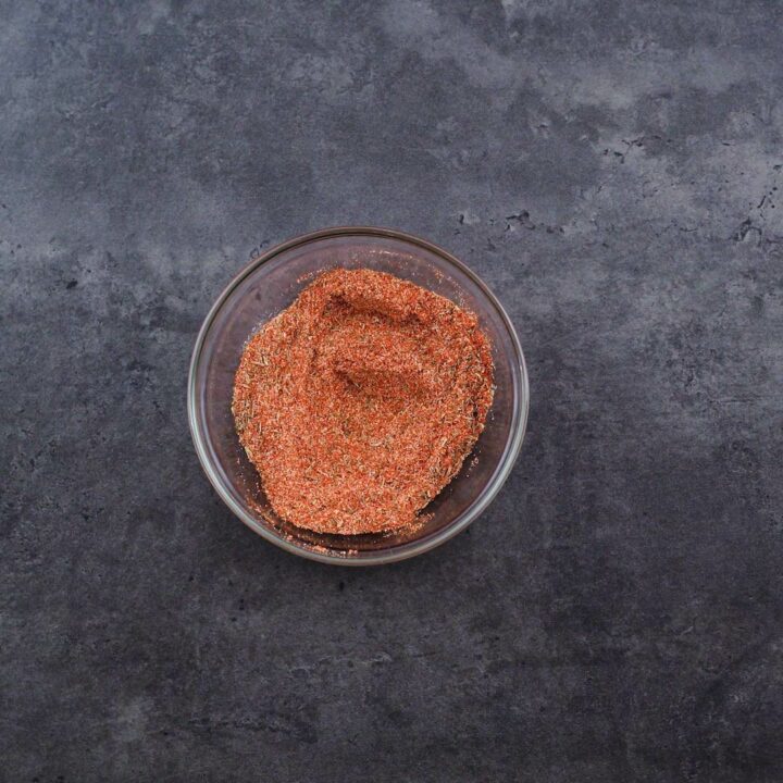 A bowl of cajun seasoning placed on agrey table.