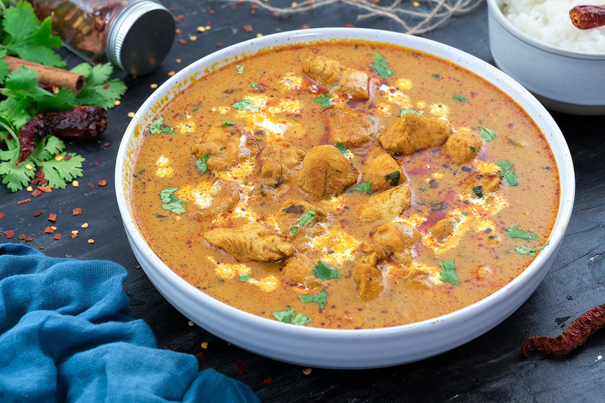 Chicken Curry in a white bowl with few ingredients around.