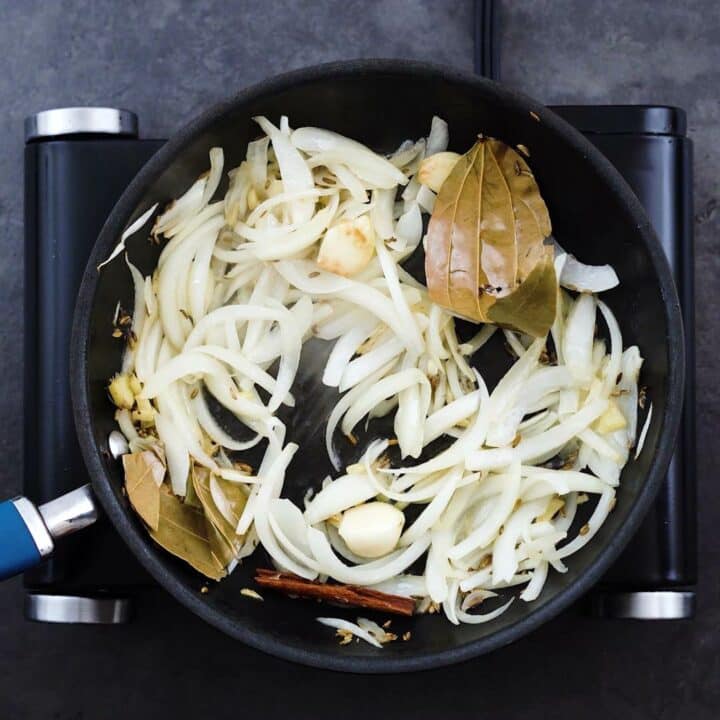 Sauteed onion with whole spices in a pan.