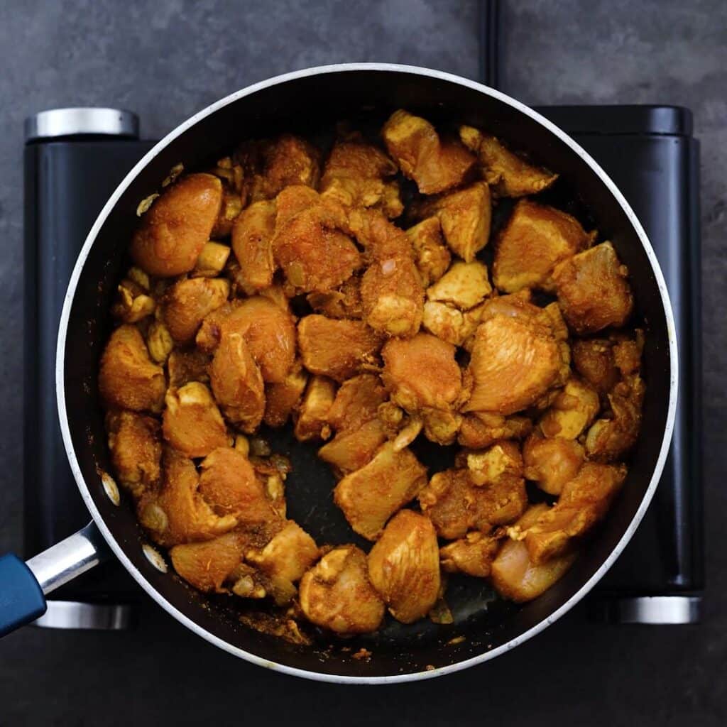 Chicken sauteed with spice powders cooking in a pan.