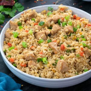A bowl of chicken fried rice with a few ingredients scattered around it.