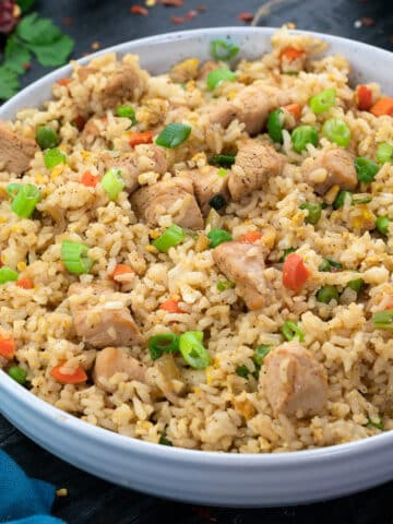 A bowl of chicken fried rice with a few ingredients scattered around it.