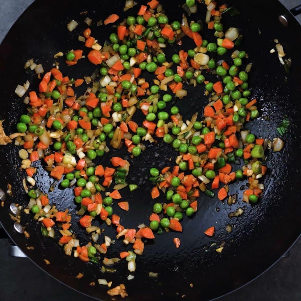 A wok containing stir-fried peas and carrots.