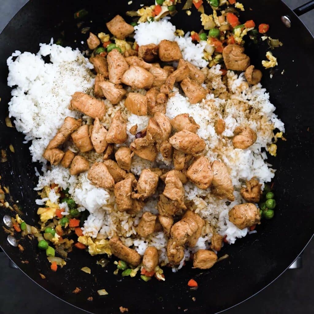 A wok containing a stir-fry of vegetables, rice, chicken, and basic seasonings.