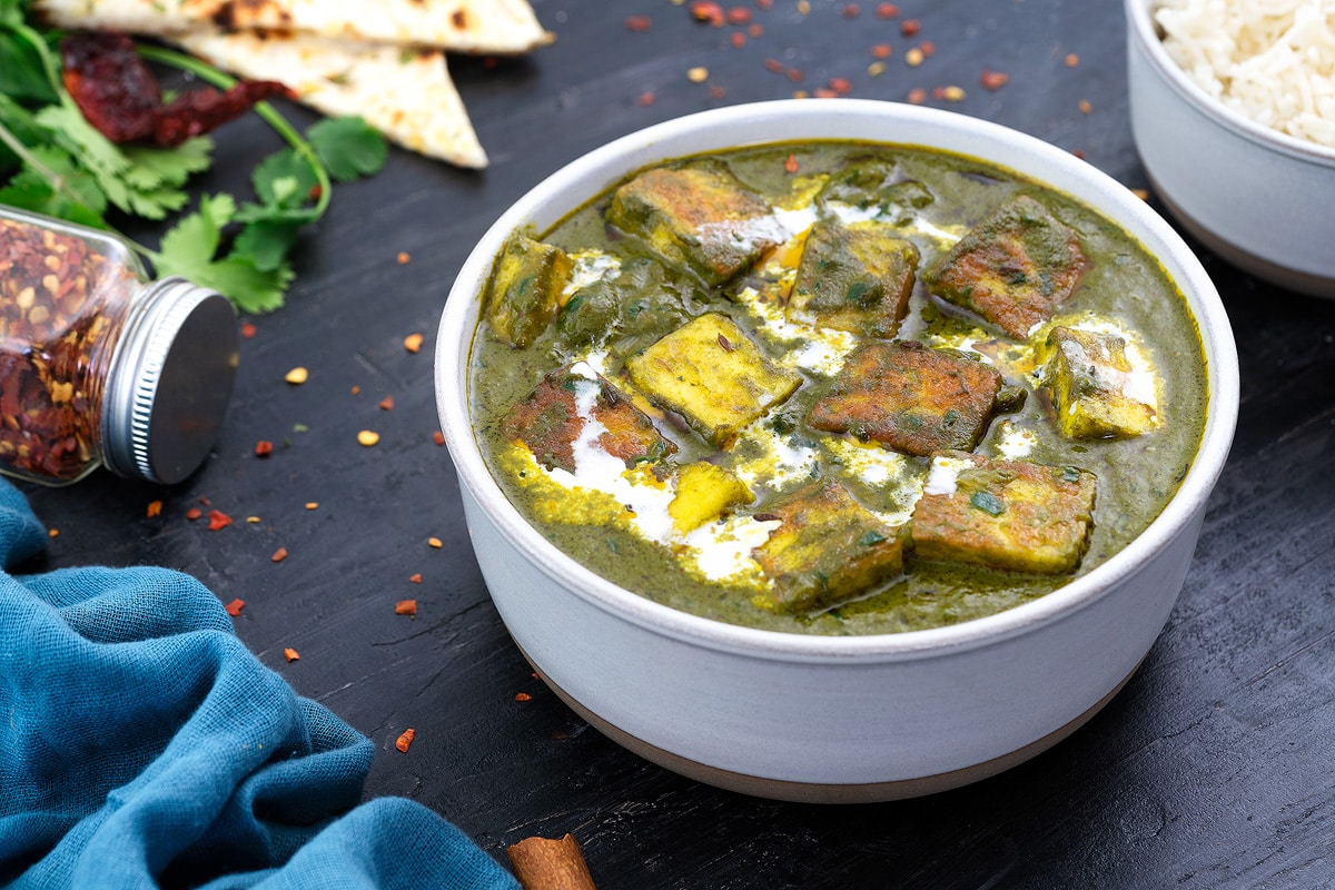 A bowl of saag paneer, surrounded by a bowl of rice and a piece of naan bread.