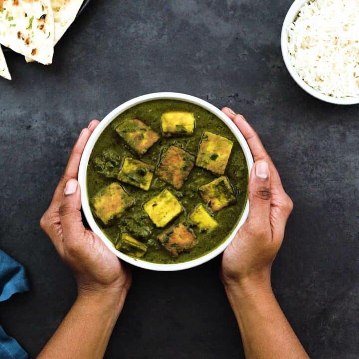Serving Saag paneer in a white bowl with rice and naan alongside.