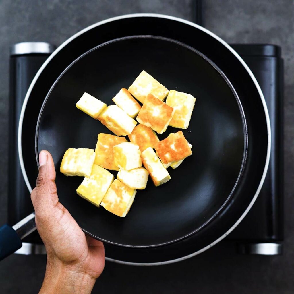 Crispy golden fried paneer on a black plate.