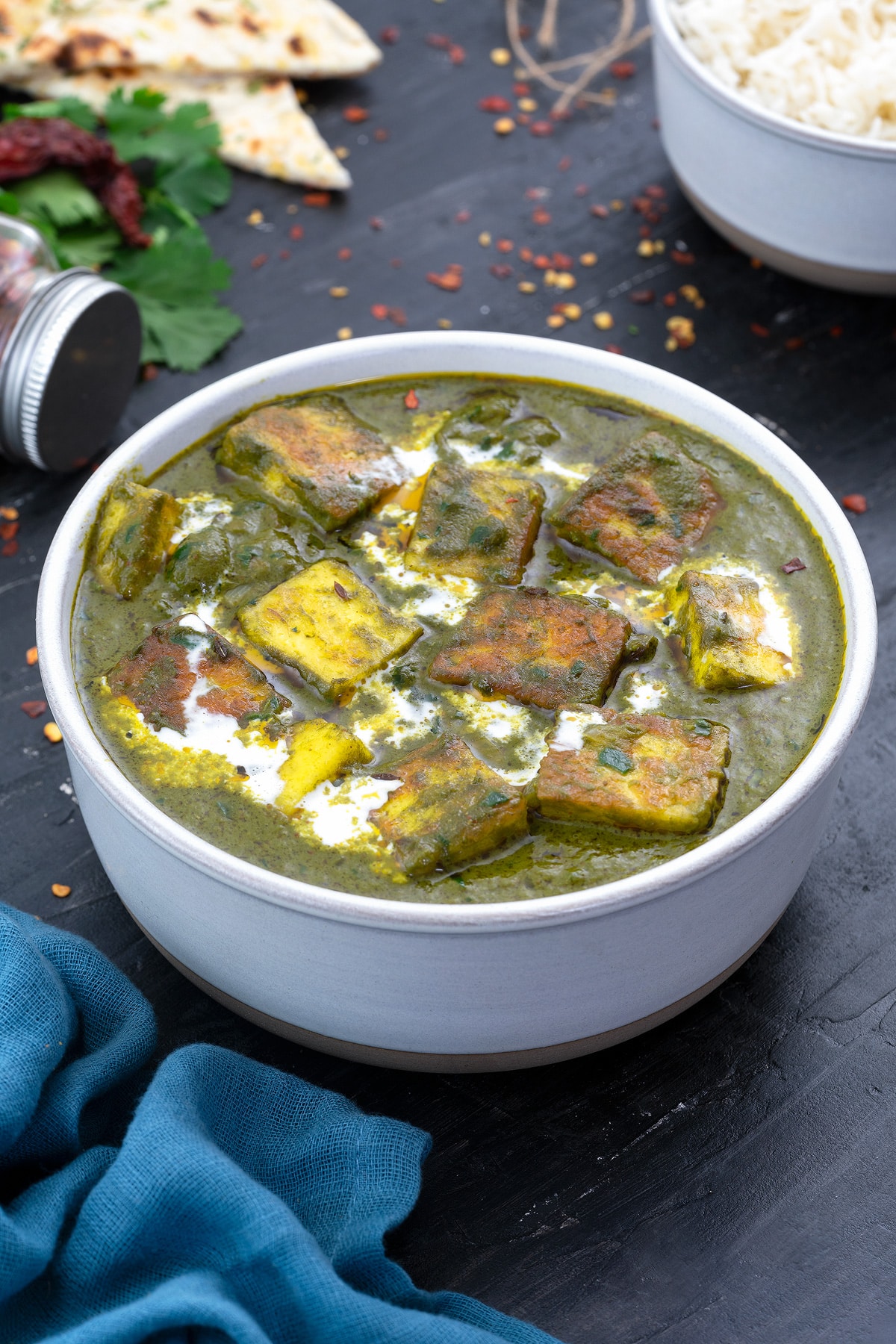 A bowl of saag paneer, surrounded by a bowl of rice and a piece of naan bread.