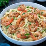 Shrimp Fettuccine Alfredo Pasta in a white bowl with few ingredients around.