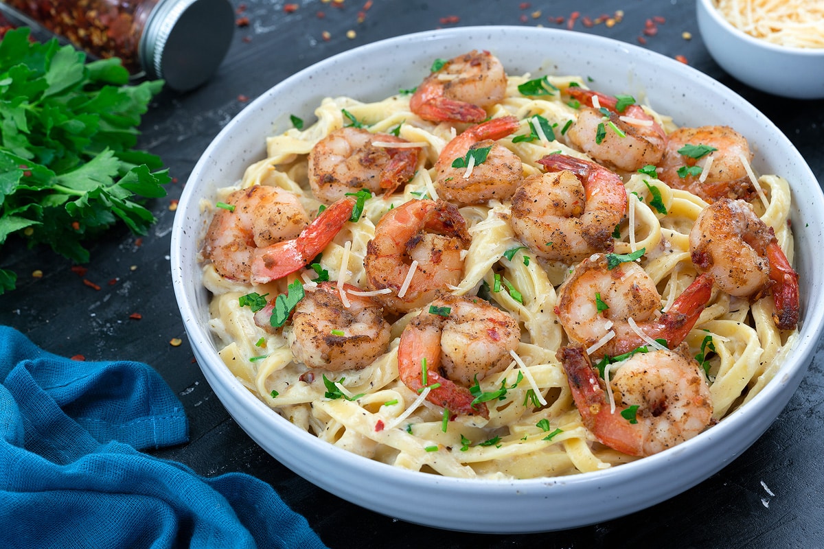 Shrimp Fettuccine Alfredo Pasta in a white bowl with few ingredients around.