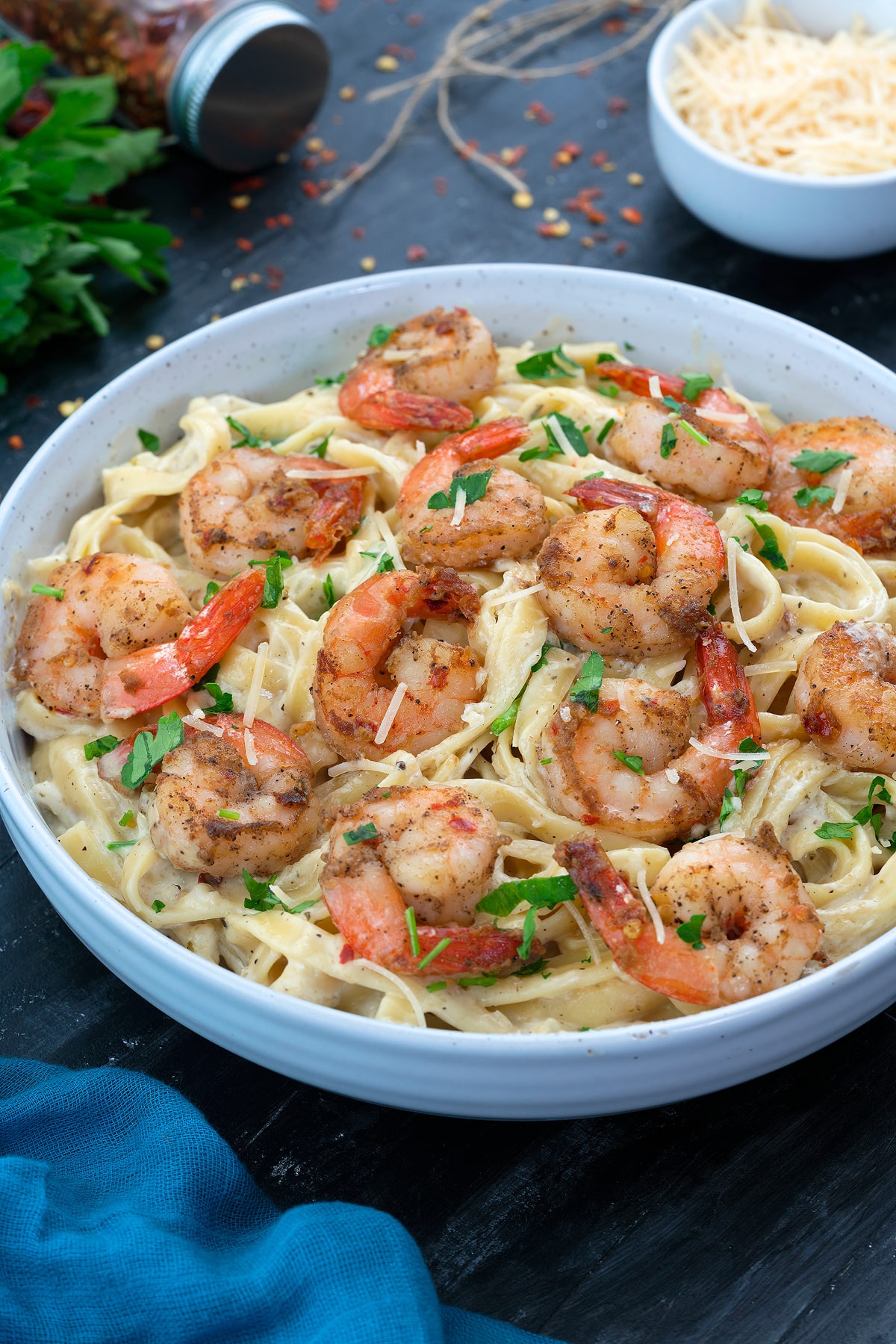 Shrimp Fettuccine Alfredo Pasta in a white bowl with few ingredients around.