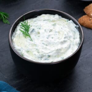 Homemade Tzatziki Sauce in a black bowl with few ingredients around.