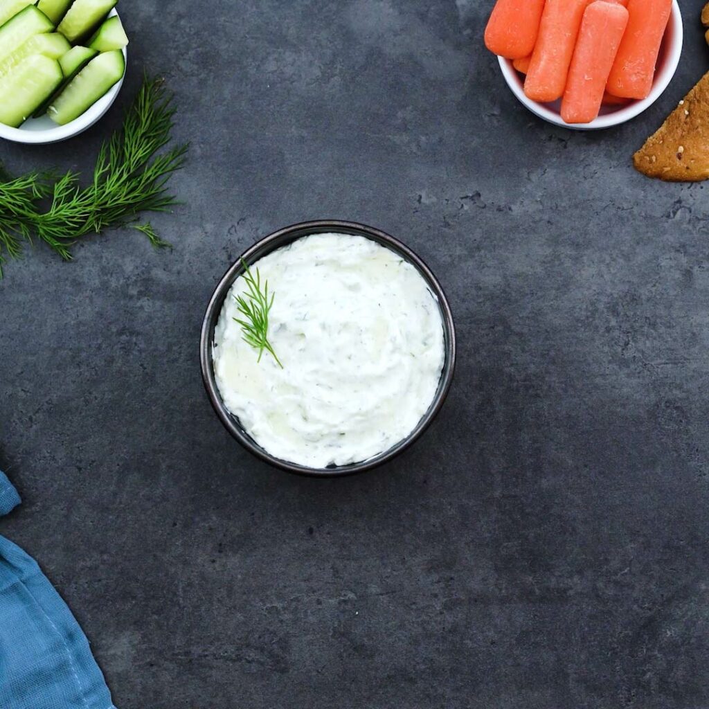 Tzatziki Sauce served in a black bowl with veggies nearby.