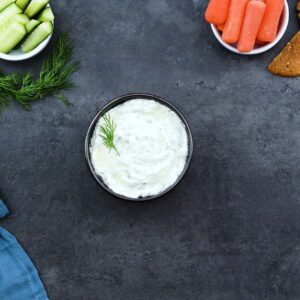 Tzatziki Sauce served in a black bowl with veggies nearby.