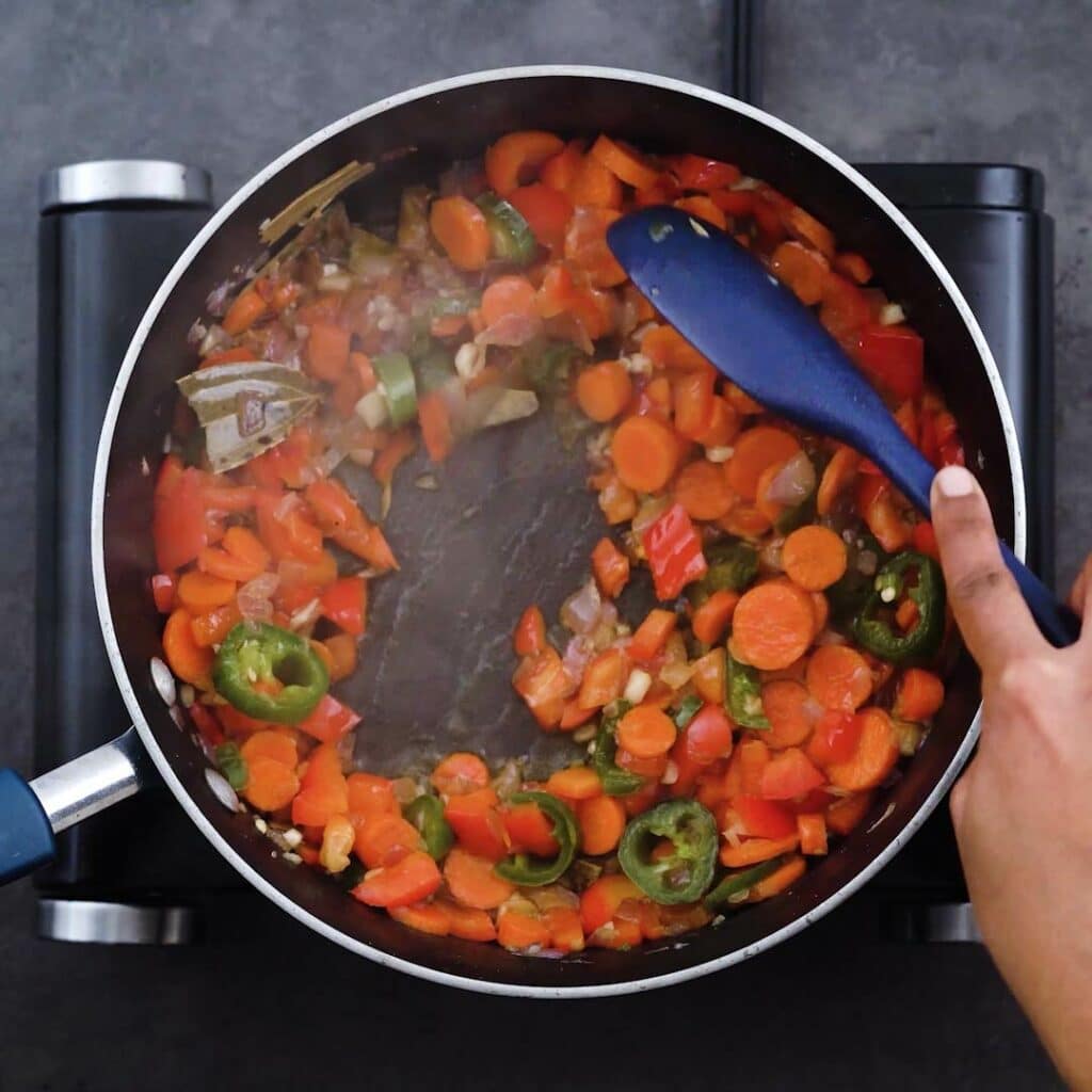 Sauteing carrots and red bell peppers in a pan.
