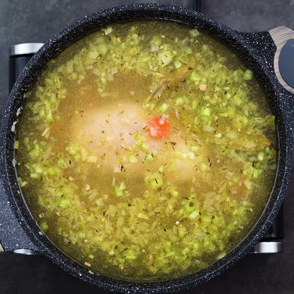 Soup mixture with chicken breast simmering in a pan.