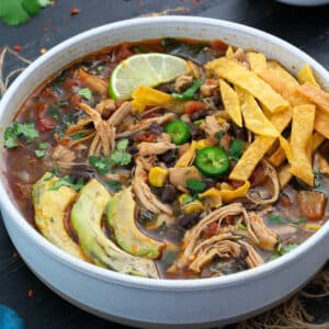 Chicken Tortilla Soup in a white bowl with avocado, lime slice and tortilla chips.