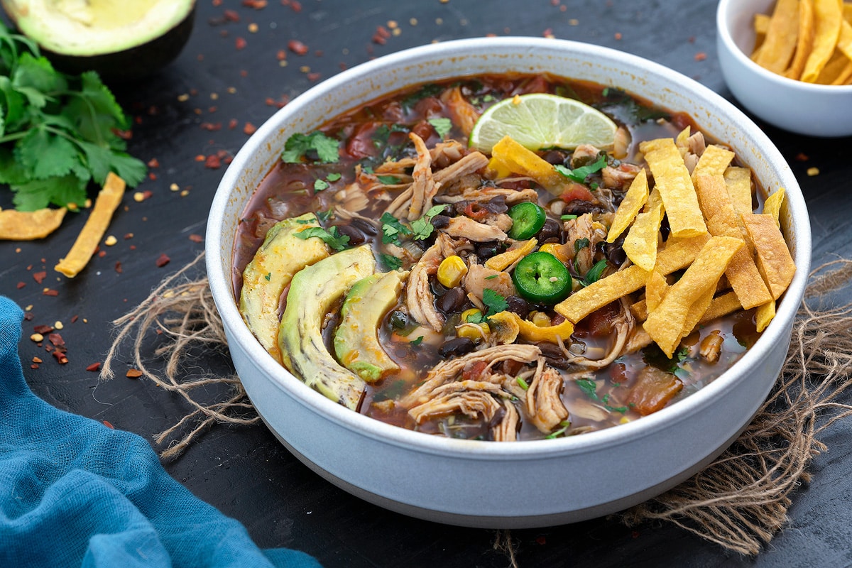 Chicken Tortilla Soup in a white bowl with avocado, lime slice and tortilla chips.