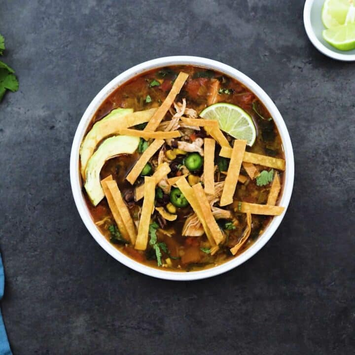 Chicken tortilla soup topped with tortilla strips, lime wedges, avocado and jalapeno slices.