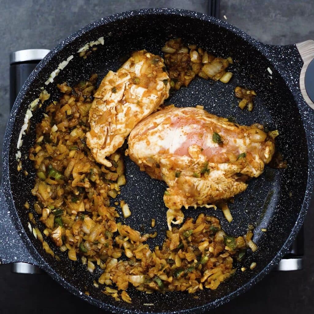 A pan with chicken breast and seasoned onion mixture.