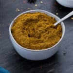 Curry Powder in a white bowl with few ingredients scattered around.
