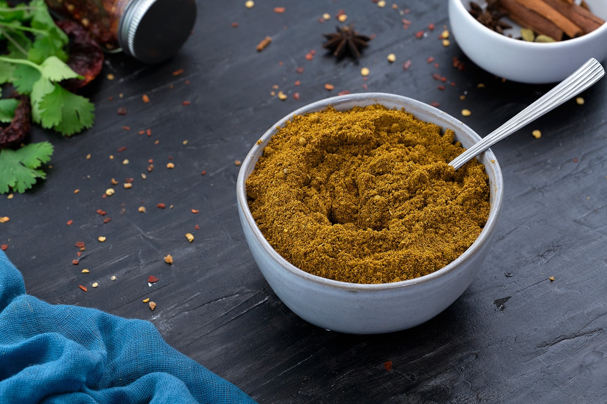 Curry Powder in a white bowl with few ingredients scattered around.