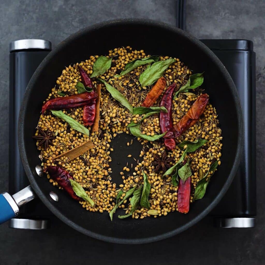 Toasted Indian whole spices and curry leaves in a pan.