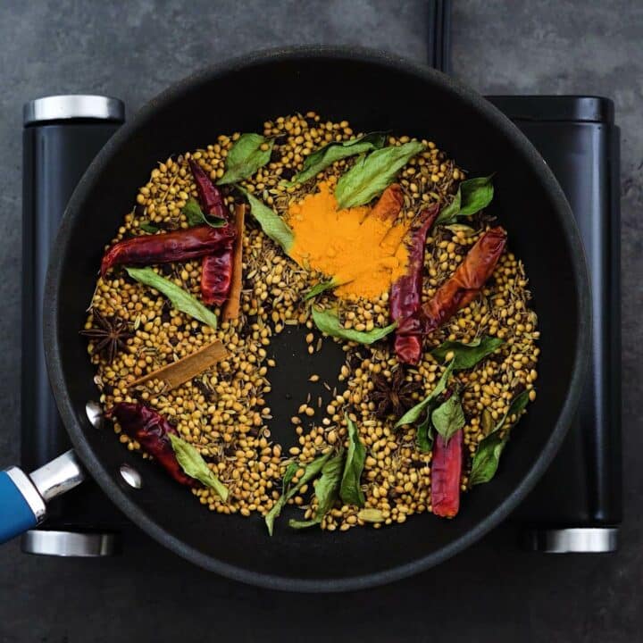 Toasted whole spices and turmeric powder in a pan.