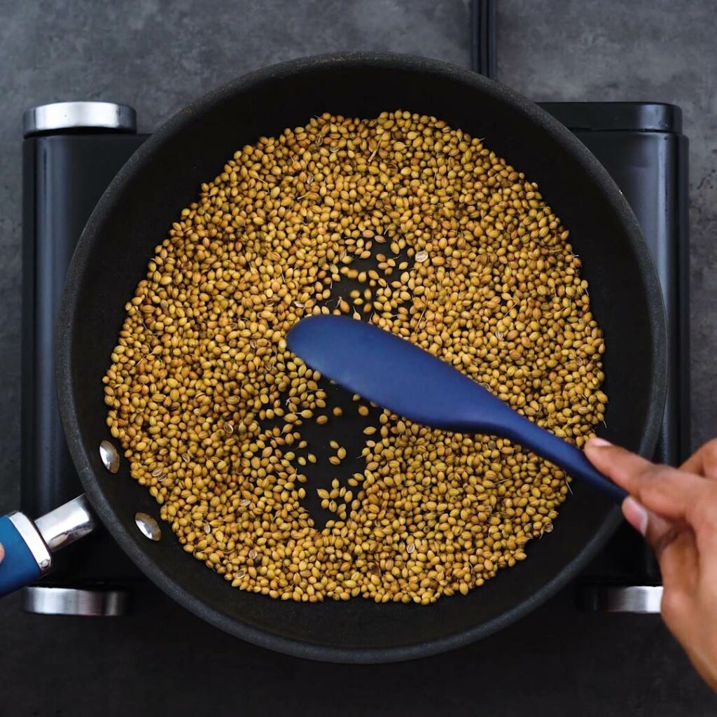 Roasting coriander seeds in a frying pan.