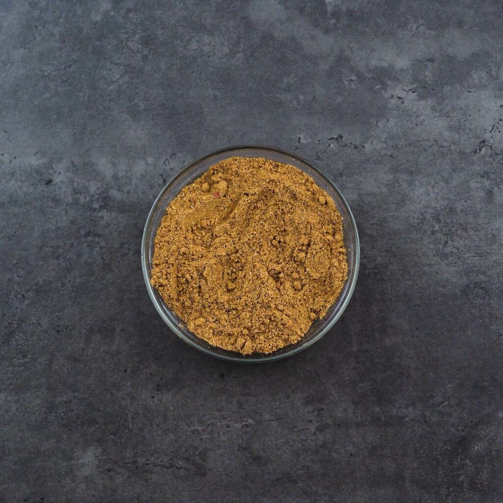A bowl of Garam Masala placed on a grey table.