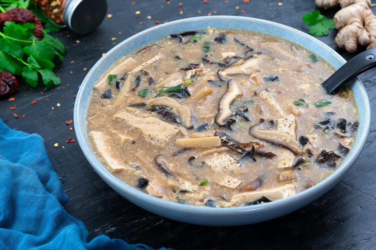 A bowl of hot and sour soup with ingredients scattered around.