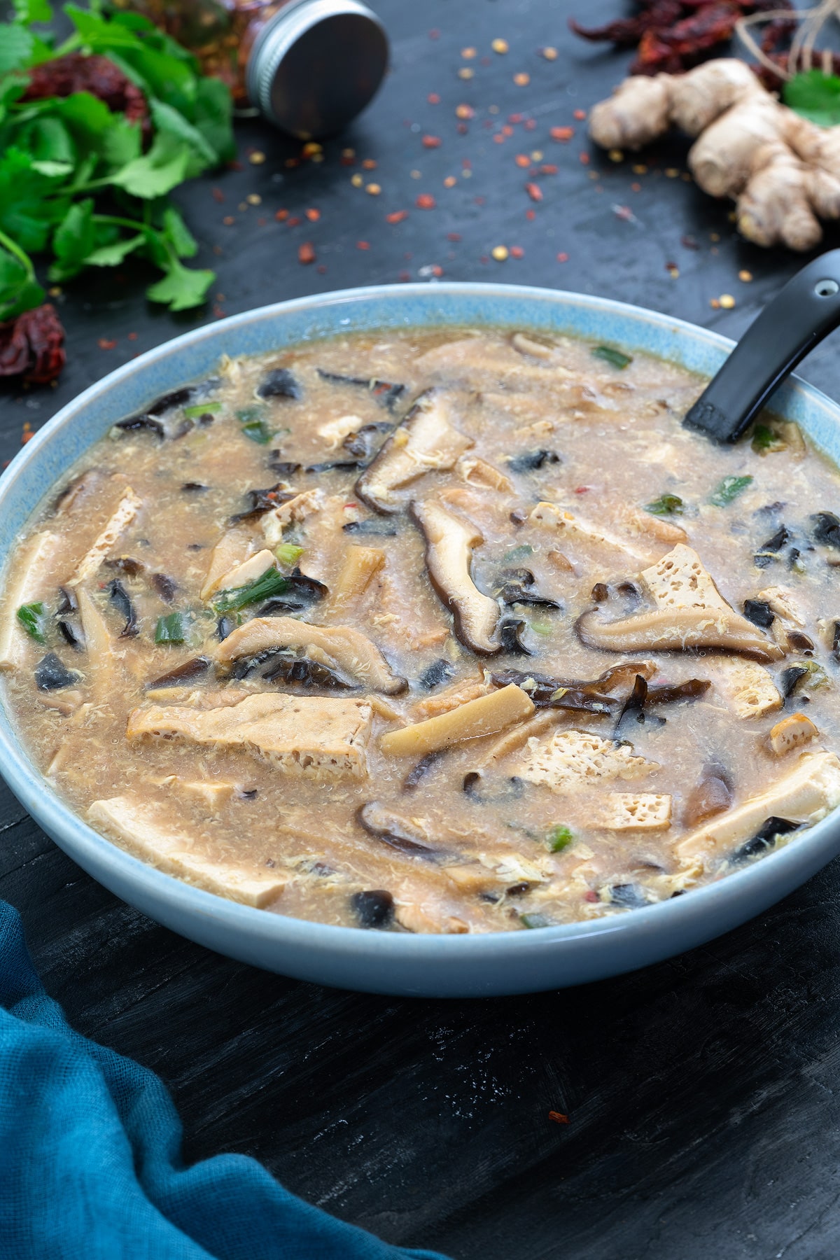 A bowl of hot and sour soup with ingredients scattered around.