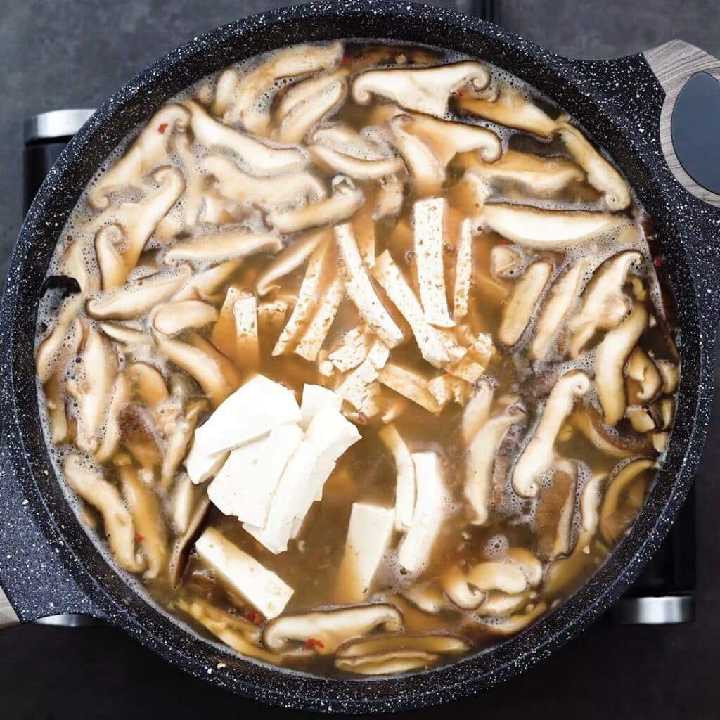 A pot with soup mixture of mushroom and tofu is boiling.