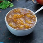 Mango Chutney in a white bowl with few ingredients scattered around.