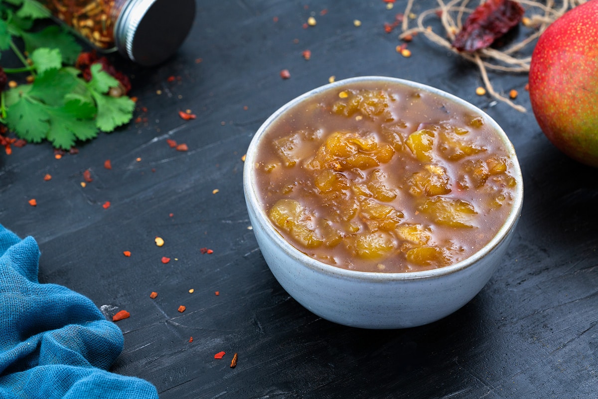 Mango Chutney in a white bowl with few ingredients scattered around.