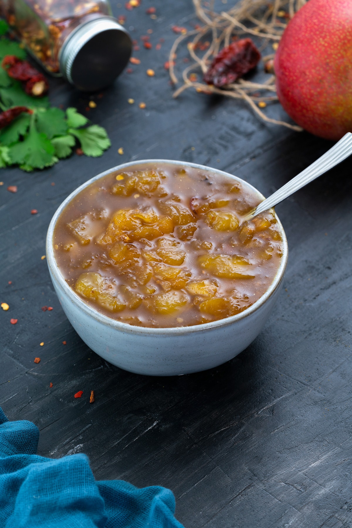 Mango Chutney in a white bowl with few ingredients scattered around.