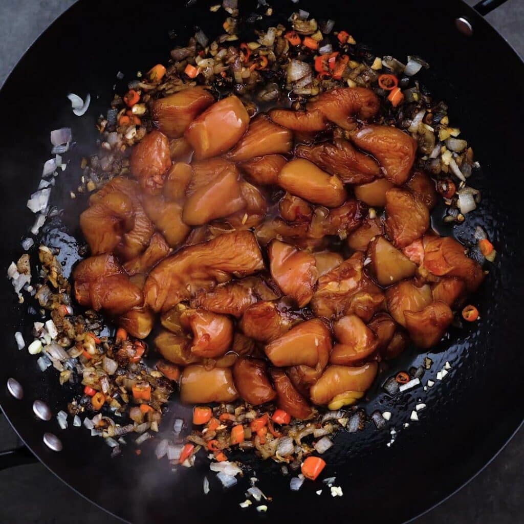 A wok with marinated chicken and aromatics.
