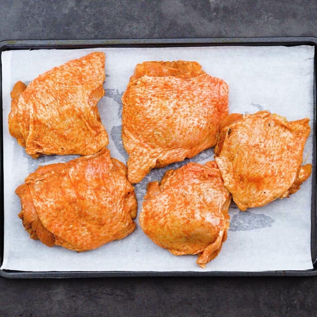 Chicken Thighs placed on a baking tray lined with parchment paper.