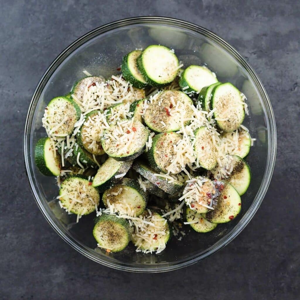 A bowl of Zucchini with seasoning and cheese.