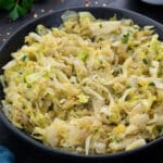 Sautéed Cabbage in a black bowl with few ingredients scattered around.