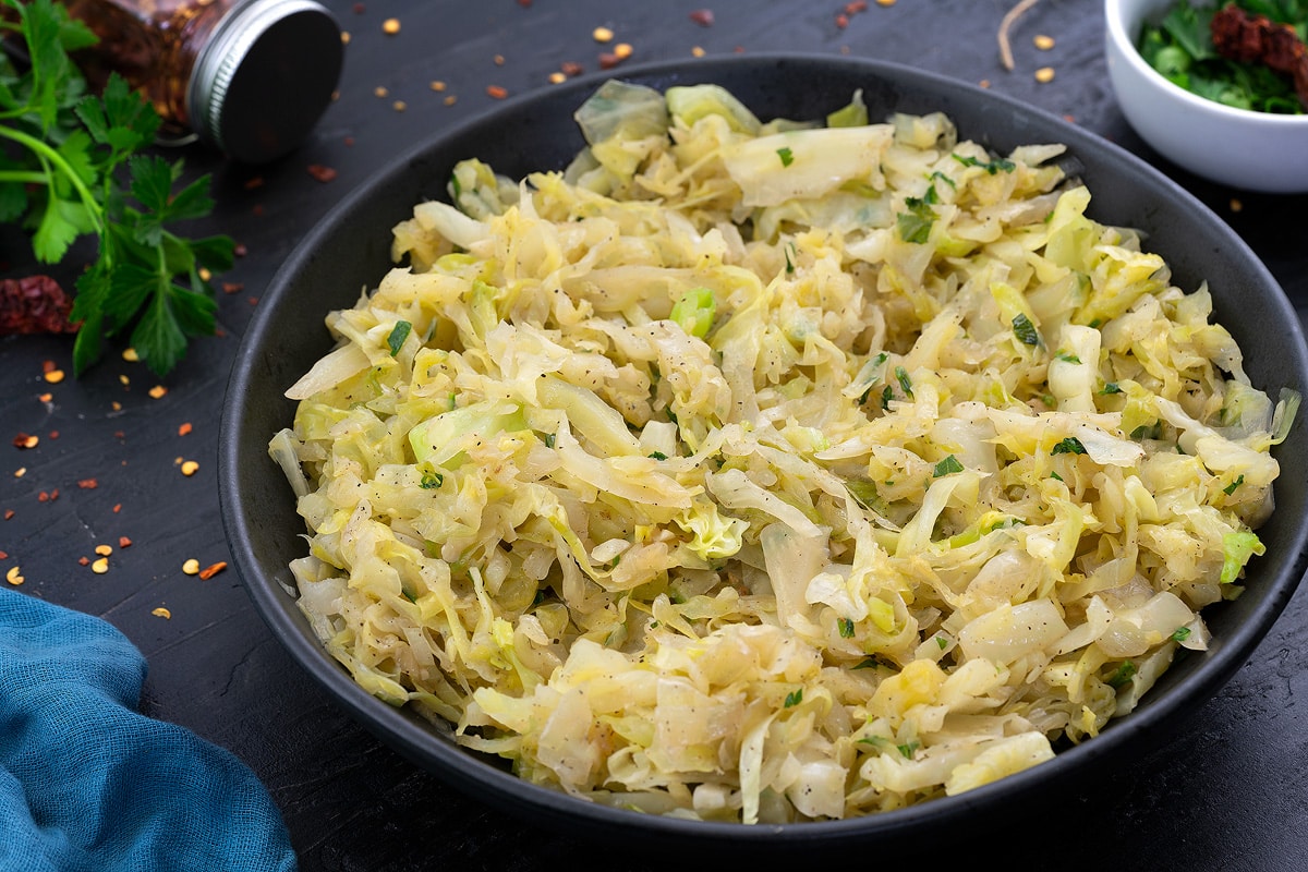 Sautéed Cabbage in a black bowl with few ingredients scattered around.